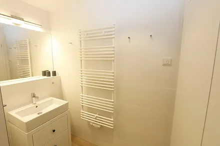 Badezimmer mit ebenerdiger Regendusche, Waschtisch, WC, Fön, Kosmetikspiegel und einem Handtuchtrockner  