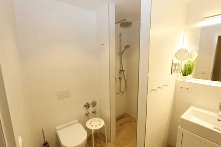 Badezimmer mit ebenerdiger Regendusche, Waschtisch, WC, Fön, Kosmetikspiegel und einem Handtuchtrockner  