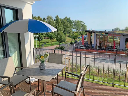 überdachter Balkon (Ost) mit Sitzgarnitur, Sonnenschirm und Blick auf die Strandpromenade und Ostsee