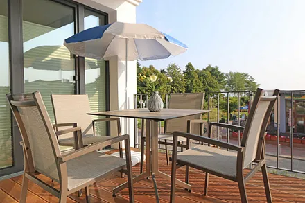 überdachter Balkon (Ost) mit Sitzgarnitur, Sonnenschirm und Blick auf die Strandpromenade und Ostsee