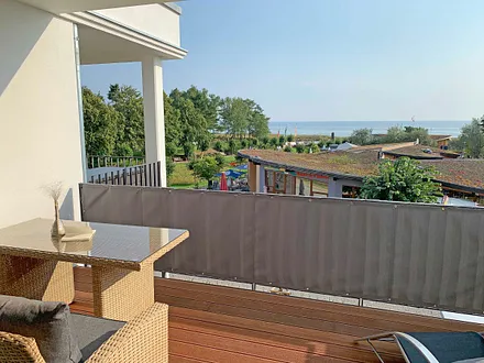 überdachter Balkon (Südost) mit Outdoorcouch, Esstisch, Liege, Sonnenschirm und freien Blick auf die Ostsee