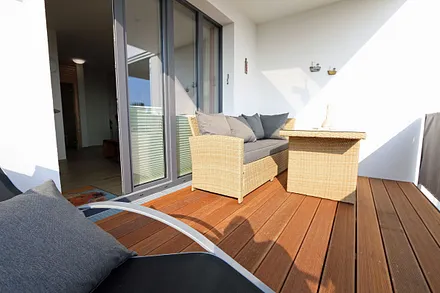 überdachter Balkon (Südost) mit Outdoorcouch, Esstisch, Liege, Sonnenschirm und freien Blick auf die Ostsee
