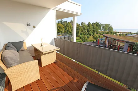 überdachter Balkon (Südost) mit Outdoorcouch, Esstisch, Liege, Sonnenschirm und freien Blick auf die Ostsee