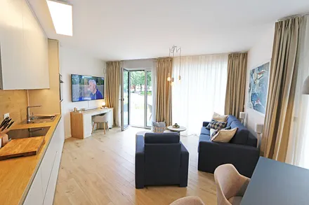 gemütlicher Wohn-/ Essbereich mit hellen Eichenholz Möbeln, Sessel, Couch mit Leselampe, Beistelltische, Stehlampe & 65“ Smart-TV 