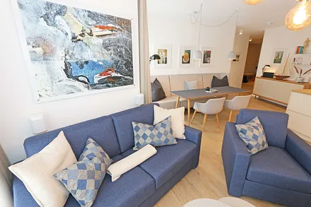 gemütlicher Wohn-/ Essbereich mit hellen Eichenholz Möbeln, Sessel, Couch mit Leselampe, Beistelltische, Stehlampe & 65“ Smart-TV 