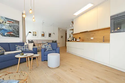 gemütlicher Wohn-/ Essbereich mit hellen Eichenholz Möbeln, Sessel, Couch mit Leselampe, Beistelltische, Stehlampe & 65“ Smart-TV 