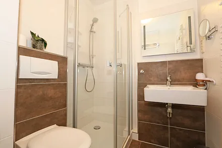 Badezimmer mit ebenerdiger Dusche, Waschplatz, WC, Handtuchheizkörper, Kosmetikspiegel und Fön