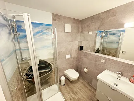 innenliegendes Badezimmer mit WC, Dusche, Waschtisch mit Unterschrank, Fön, Kosmetikspiegel, großem Wandspiegel, Handtuchheizkörper und einem Ablageregal