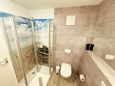 innenliegendes Badezimmer mit WC, Dusche, Waschtisch mit Unterschrank, Fön, Kosmetikspiegel, großem Wandspiegel, Handtuchheizkörper und einem Ablageregal