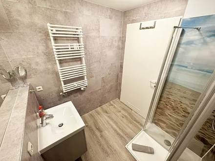 innenliegendes Badezimmer mit WC, Dusche, Waschtisch mit Unterschrank, Fön, Kosmetikspiegel, großem Wandspiegel, Handtuchheizkörper und einem Ablageregal