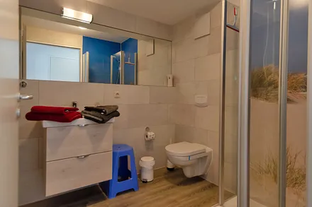 innenliegendes Badezimmer mit WC, Dusche, Waschtisch mit Unterschrank, Fön, Kosmetikspiegel, großem Wandspiegel, Handtuchheizkörper und einem Ablageregal