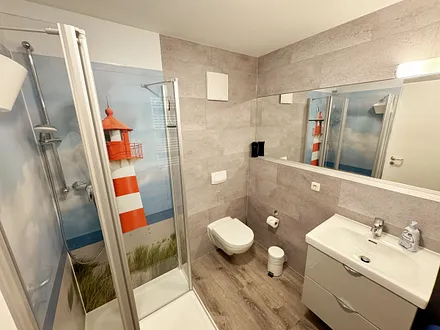 innenliegendes Badezimmer mit WC, Dusche, Waschtisch mit Unterschrank, Fön, Kosmetikspiegel, großem Wandspiegel, Handtuchheizkörper und einem Ablageregal