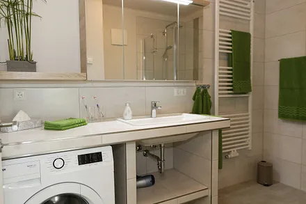 modernes Badezimmer mit ebenerdiger komfortabler Regendusche, Waschplatz, WC, Kosmetikspiegel, Fön, Spiegelschrank und einen Handtuchtrockner