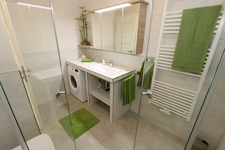 modernes Badezimmer mit ebenerdiger komfortabler Regendusche, Waschplatz, WC, Kosmetikspiegel, Fön, Spiegelschrank und einen Handtuchtrockner