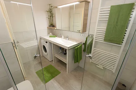 modernes Badezimmer mit ebenerdiger komfortabler Regendusche, Waschplatz, WC, Kosmetikspiegel, Fön, Spiegelschrank und einen Handtuchtrockner