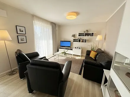 Wohnbereich mit modernen weißen Hülsta Möbeln, ein gemütliches Ledersofa, zwei Sessel, zwei Couchtischen, Stehlampen, DAB Radio mit CD-Player und Bluetooth, Smart-TV mit Soundbar & Blu-Ray Player