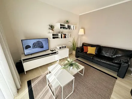 Wohnbereich mit modernen weißen Hülsta Möbeln, ein gemütliches Ledersofa, zwei Sessel, zwei Couchtischen, Stehlampen, DAB Radio mit CD-Player und Bluetooth, Smart-TV mit Soundbar & Blu-Ray Player