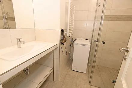 modernes Badezimmer mit ebenerdiger Glasdusche, Waschplatz, WC, Fön, Handtuchtrockner und Waschmaschine