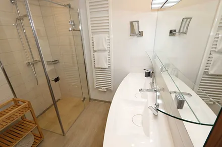 Badezimmer mit Regendusche, großzügigem Doppelwaschtisch, großem Spiegel, Kosmetikspiegel, Handtuchtrockner und Fön