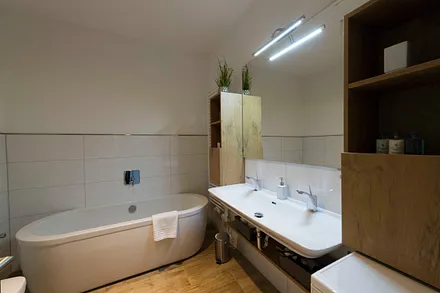 Badezimmer mit ebenerdiger, komfortabler Regendusche mit Echtglasabtrennung, Fön, Kosmetikspiegel, Waschplatz mit Unterschrank sowie freistehender Badewanne