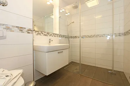 Badezimmer mit ebenerdiger und geräumiger Regen-Dusche, Waschplatz, WC, Fön, Kosmetikspiegel sowie einen Handtuchheizkörper