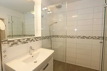 Badezimmer mit ebenerdiger und geräumiger Regen-Dusche, Waschplatz, WC, Fön, Kosmetikspiegel sowie einen Handtuchheizkörper