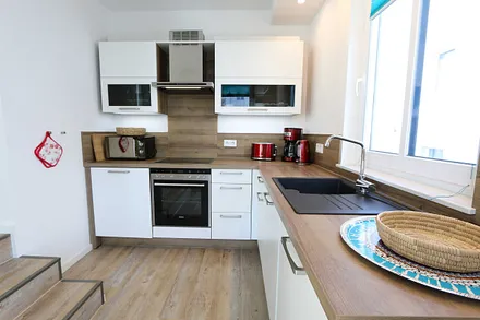 Küchenzeile mit Ceranfeld, Backofen, Geschirrspüler, Mikrowelle, Kühlschrank mit Gefrierfach, Kaffeemaschine, Wasserkocher, Toaster und diversen Küchenutensilien