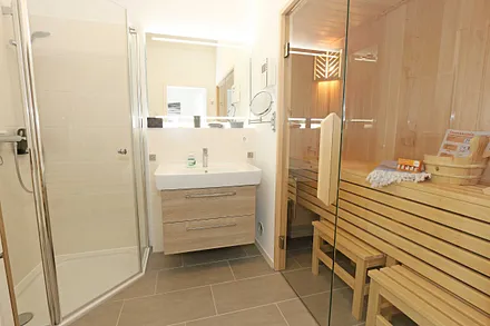 Badezimmer mit ebenerdiger Dusche, Fön, Badradio, Kosmetikspiegel, Waschtisch mit Unterschrank, WC und wohnungseigener Sauna