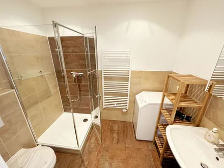 Badezimmer mit moderner Dusche mit Glasabtrennung, Handtuchheizkörper, WC, Kosmetikspiegel, Fön und Waschmaschine