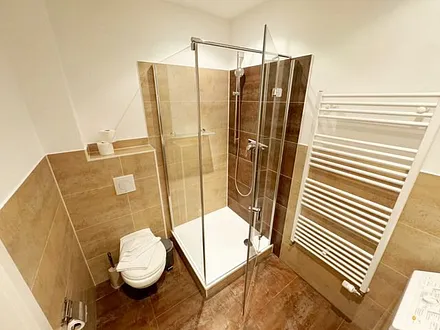 Badezimmer mit moderner Dusche mit Glasabtrennung, Handtuchheizkörper, WC, Kosmetikspiegel, Fön und Waschmaschine