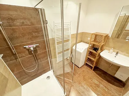 Badezimmer mit moderner Dusche mit Glasabtrennung, Handtuchheizkörper, WC, Kosmetikspiegel, Fön und Waschmaschine