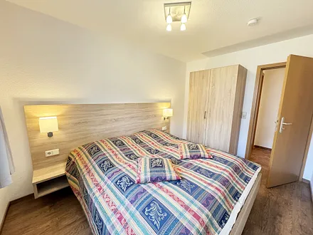 Schlafzimmer mit Doppelbett, Komfortmatratzen (2x 0,90 m x 2,00 m), Nachttischkonsolen, Kleiderschrank und Verdunklungsgardinen