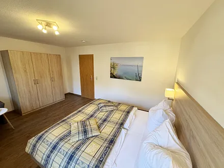 Schlafzimmer hell und modern eingerichtet mit Doppelbett, Komfortmatratzen (2x 0,90 m x 2,00 m), Nachttischkonsolen, Kleiderschrank und Verdunklungsgardinen