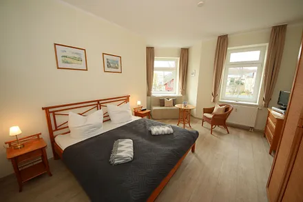 Schlafzimmer mit Doppelbett (1,80 m x 2,00 m), großem Kleiderschrank, Nachttischablagen, Kommode mit Smart-TV und komfortabler Leseecke mit kleiner Bücherauswahl