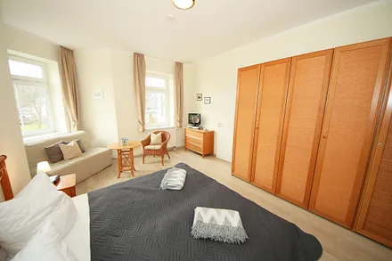 Schlafzimmer mit Doppelbett (1,80 m x 2,00 m), großem Kleiderschrank, Nachttischablagen, Kommode mit Smart-TV und komfortabler Leseecke mit kleiner Bücherauswahl