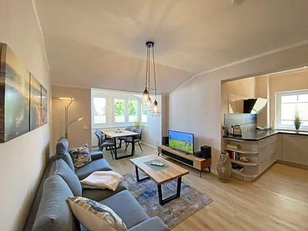 Wohnzimmer mit gemütlicher Couch, Couchtisch, Leselampe, Sessel, Hocker, Lowboard, Smart-TV, Blu-Ray Player, Teufel-Musikanlage mit Radio, DAB Radio, CD-Spieler, USB-Anschluss und Bluetooth