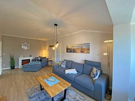 Wohnzimmer mit gemütlicher Couch, Couchtisch, Leselampe, Sessel, Hocker, Lowboard, Smart-TV, Blu-Ray Player, Teufel-Musikanlage mit Radio, DAB Radio, CD-Spieler, USB-Anschluss und Bluetooth