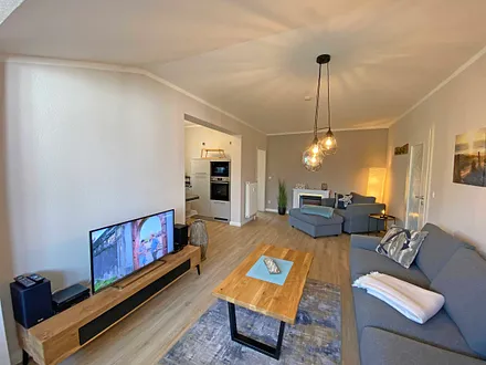 Wohnzimmer mit gemütlicher Couch, Couchtisch, Leselampe, Sessel, Hocker, Lowboard, Smart-TV, Blu-Ray Player, Teufel-Musikanlage mit Radio, DAB Radio, CD-Spieler, USB-Anschluss und Bluetooth