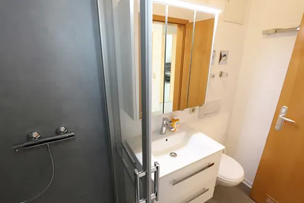 Badezimmer mit komfortabler Dusche (1,20 m x 0,80 m) mit Glasschiebetür, WC, Waschtisch, Kosmetikspiegel, Unterschrank, Spiegelschrank, Kosmetikspiegel sowie ein Fön
