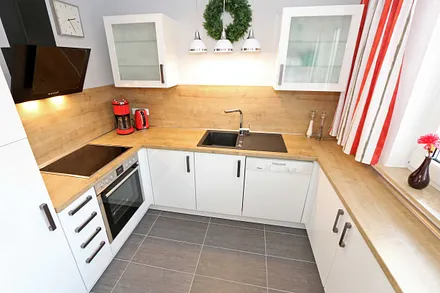 moderne Küchenzeile mit Ceranfeld, Backofen, Kühlschrank mit Eisfach, Geschirrspüler, Mikrowelle, Wasserkocher, Toaster, Kaffeemaschine und diverse Kochutensilien