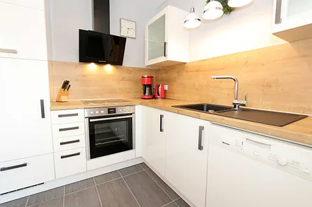 moderne Küchenzeile mit Ceranfeld, Backofen, Kühlschrank mit Eisfach, Geschirrspüler, Mikrowelle, Wasserkocher, Toaster, Kaffeemaschine und diverse Kochutensilien