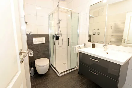 Badezimmer mit Regendusche, Waschtisch, Fön, WC, beleuchteten Spiegel sowie Handtuchheizkörper