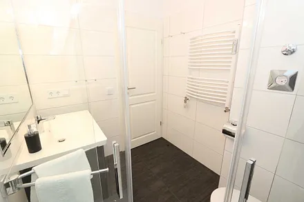 Badezimmer mit Regendusche, Waschtisch, Fön, WC, beleuchteten Spiegel sowie Handtuchheizkörper