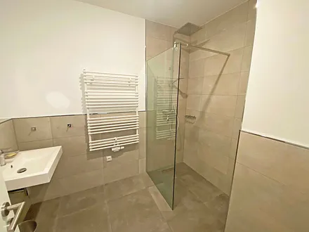 innenliegendes Bad mit einem Waschtisch, beheiztem und beleuchtetem Spiegel, Handtuchheizung, Fön, Kosmetikspiegel, WC sowie eine große ebenerdige Klarglas-Dusche mit Regenduschkopf