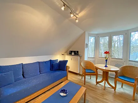 Wohnbereich mit Couch, Couchtisch sowie TV-Board, Leselampe, LCD-Flachbildschirm, Blu-Ray-Player und Mini-Stereo-Anlage sowie Insektenschutzgitter