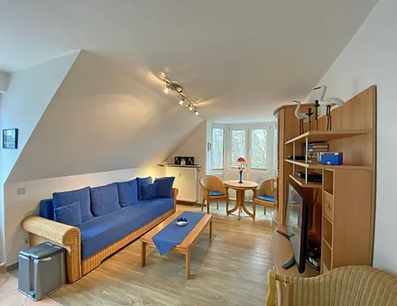 Wohnbereich mit Couch, Couchtisch sowie TV-Board, Leselampe, LCD-Flachbildschirm, Blu-Ray-Player und Mini-Stereo-Anlage sowie Insektenschutzgitter