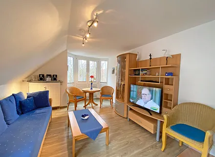 Wohnbereich mit Couch, Couchtisch sowie TV-Board, Leselampe, LCD-Flachbildschirm, Blu-Ray-Player und Mini-Stereo-Anlage sowie Insektenschutzgitter