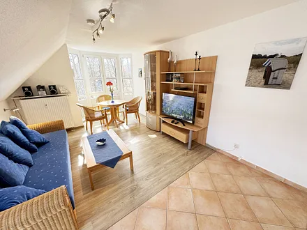 Wohnbereich mit Couch, Couchtisch sowie TV-Board, Leselampe, LCD-Flachbildschirm, Blu-Ray-Player und Mini-Stereo-Anlage sowie Insektenschutzgitter