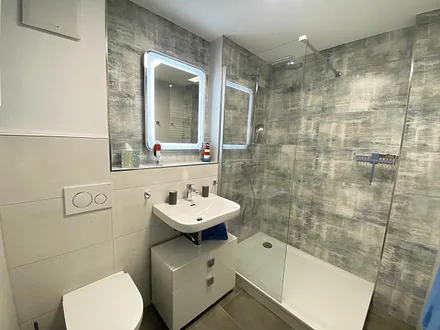 Badezimmer mit offener Glasdusche (niedriger Einstieg), Waschplatz, WC, Kosmetikspiegel, Fön sowie einem Handtuchtrockner und Fußbodenheizung 