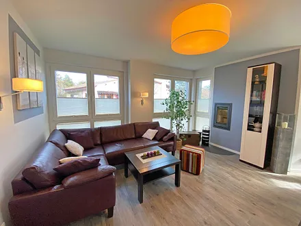 lichtdurchfluteter Wohnbereich mit Kamin, große Ledercouch, Couchtisch mit Hocker, Sideboard, Vitrine, Smart-TV mit Blu-Ray-Player sowie eine kleine Auswahl an Urlaubslektüre und CD`s